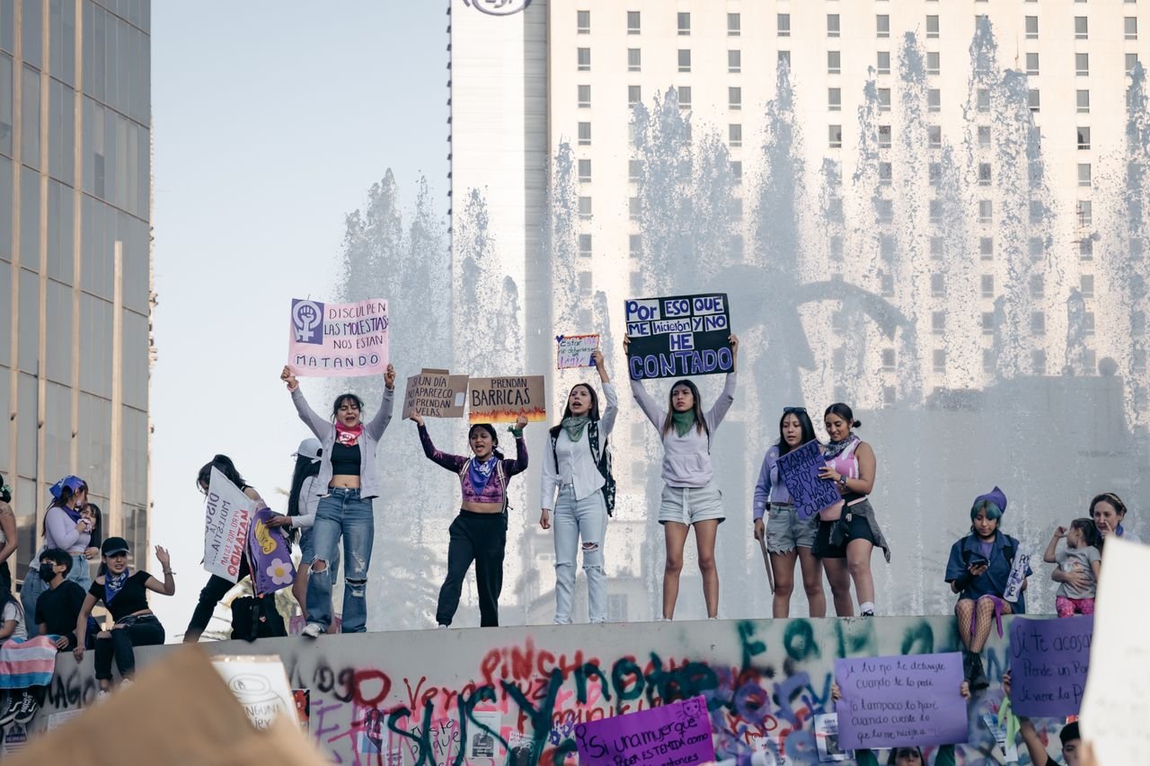 who-we-are Women protesting in Mexico City holding signs for rights and equality. Urban setting with strong group presence.