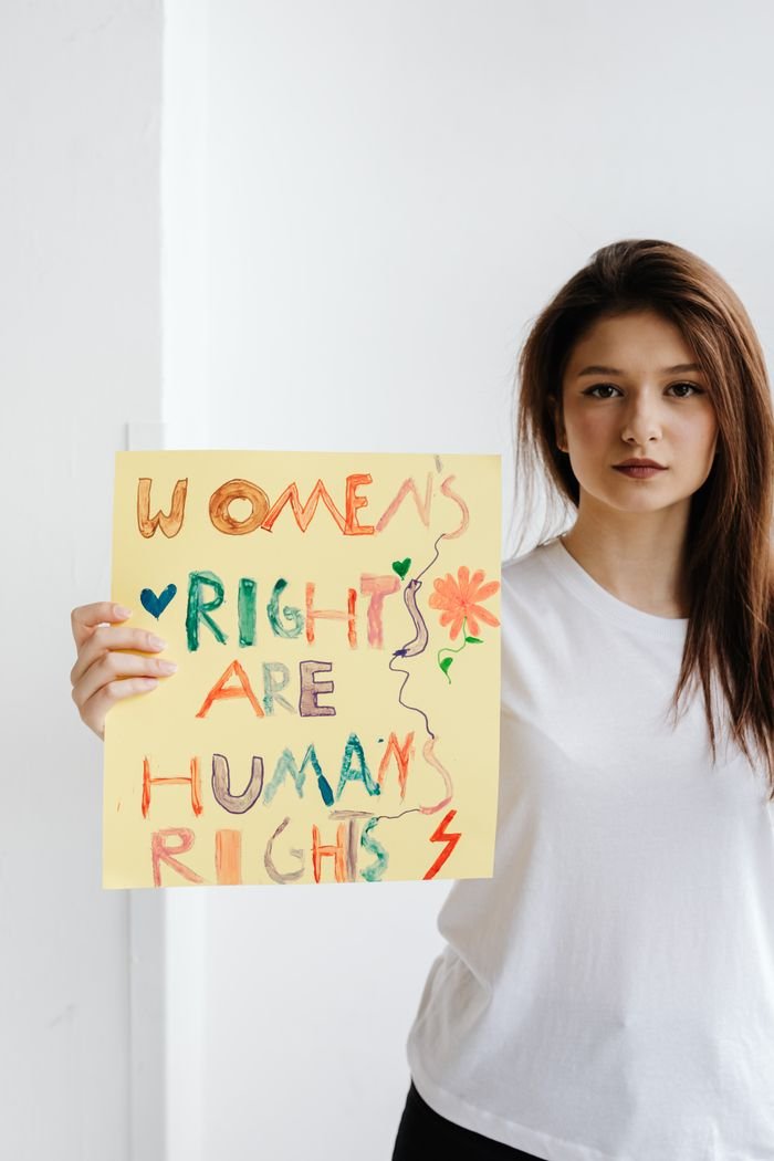 services-04 Young woman holding a colorful poster indoors advocating for women's and human rights.